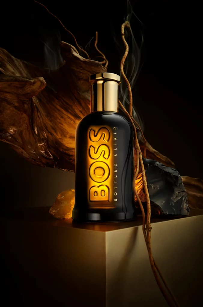 A brown bottle of BOSS elixir fragrance sits against a glowing wood ember.