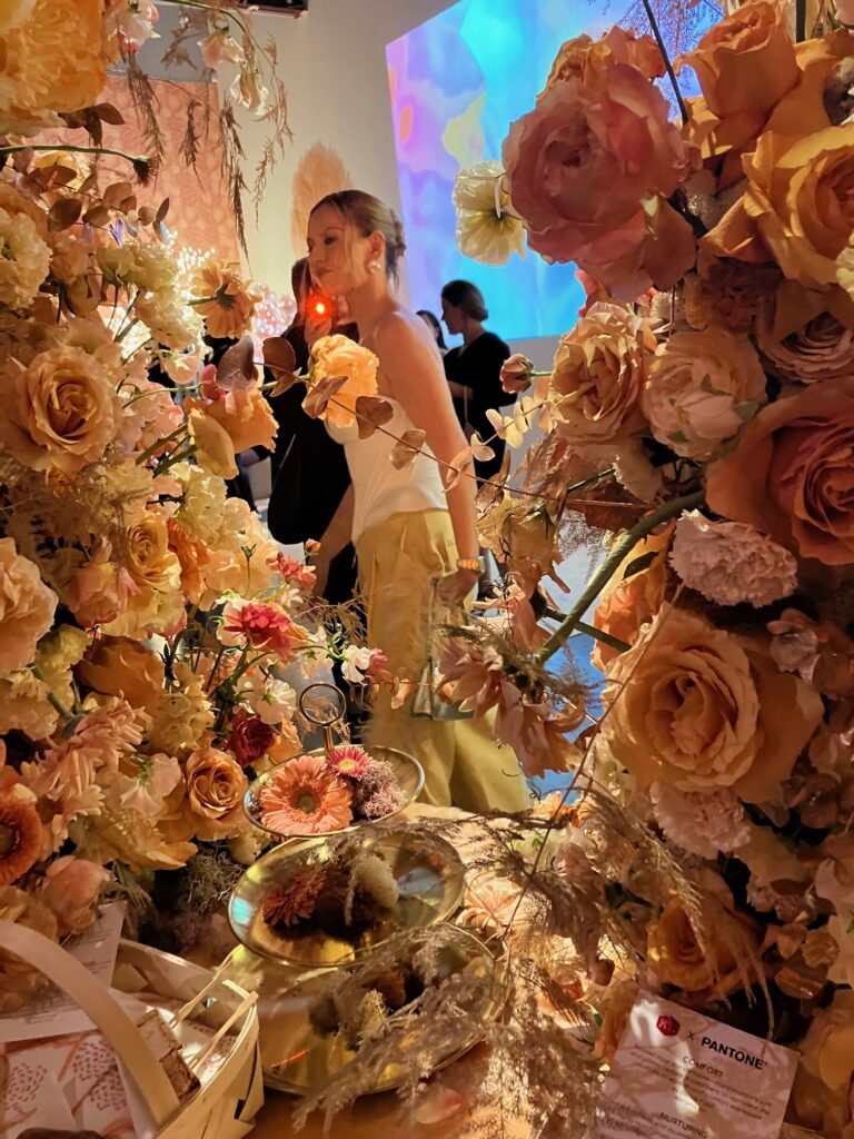 A woman in a dress wals through a display of peach colored flowers that fill the frame.