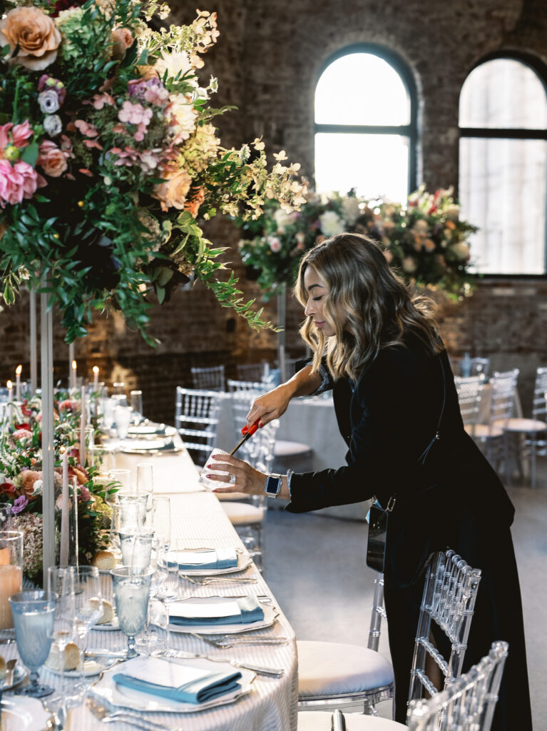 A woman lights candles on a white table with plenty of flowers and candles decorating the table.