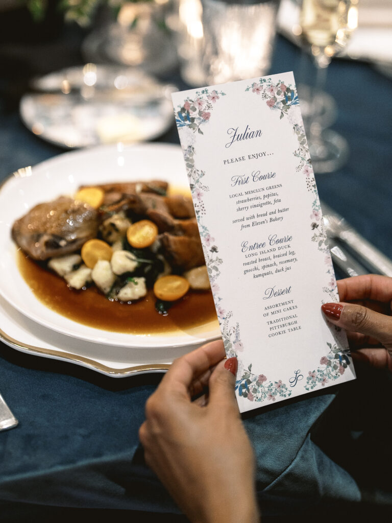 A white plate holds the dinner at a wedding reception while a person holds the menu in front of the plate.