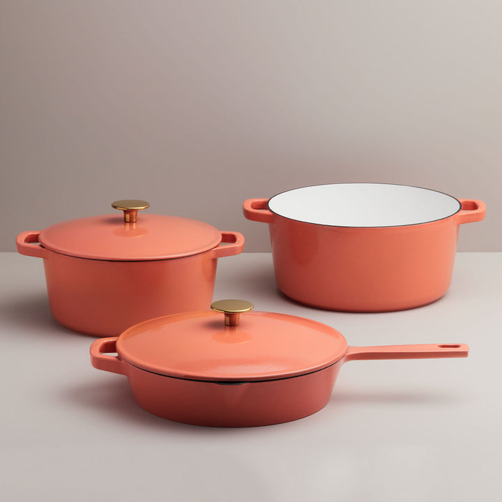 A three piece set of cookware of two dutch ovens and a big pan in a dark shade of coral.