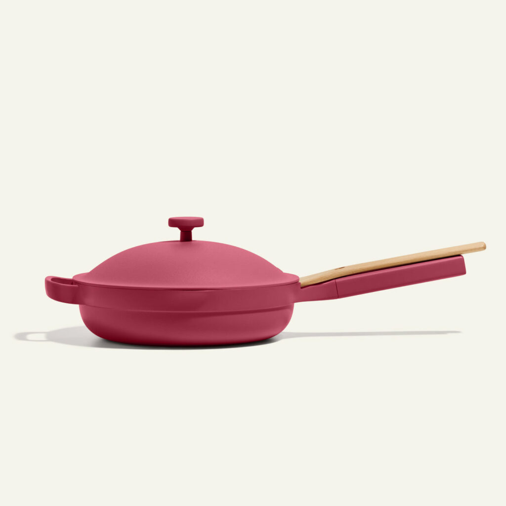 A pink pan with a lid sits on a white background to showcase stylish cookware from Our Place.