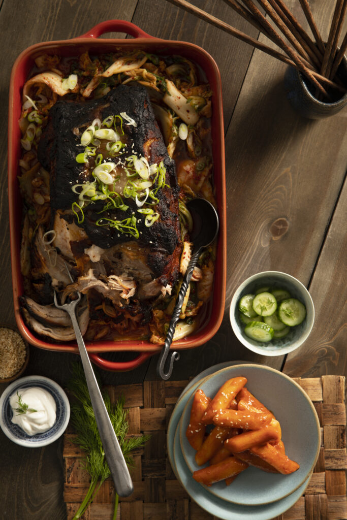 A tantalizinbraised pork shoulder & kimchi soup featuring Korean flavors, garnished with fresh dill, sour cream, scallions, and toasted sesame seeds.