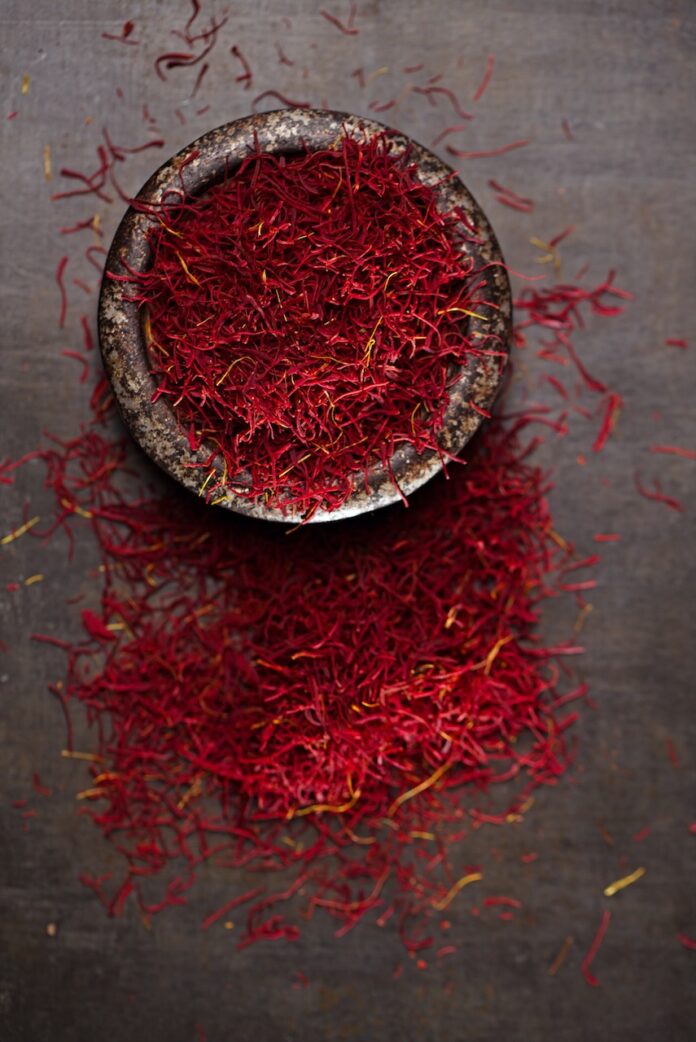 saffron spice threads and powder in a vintage iron dish on a old metal background, closeup