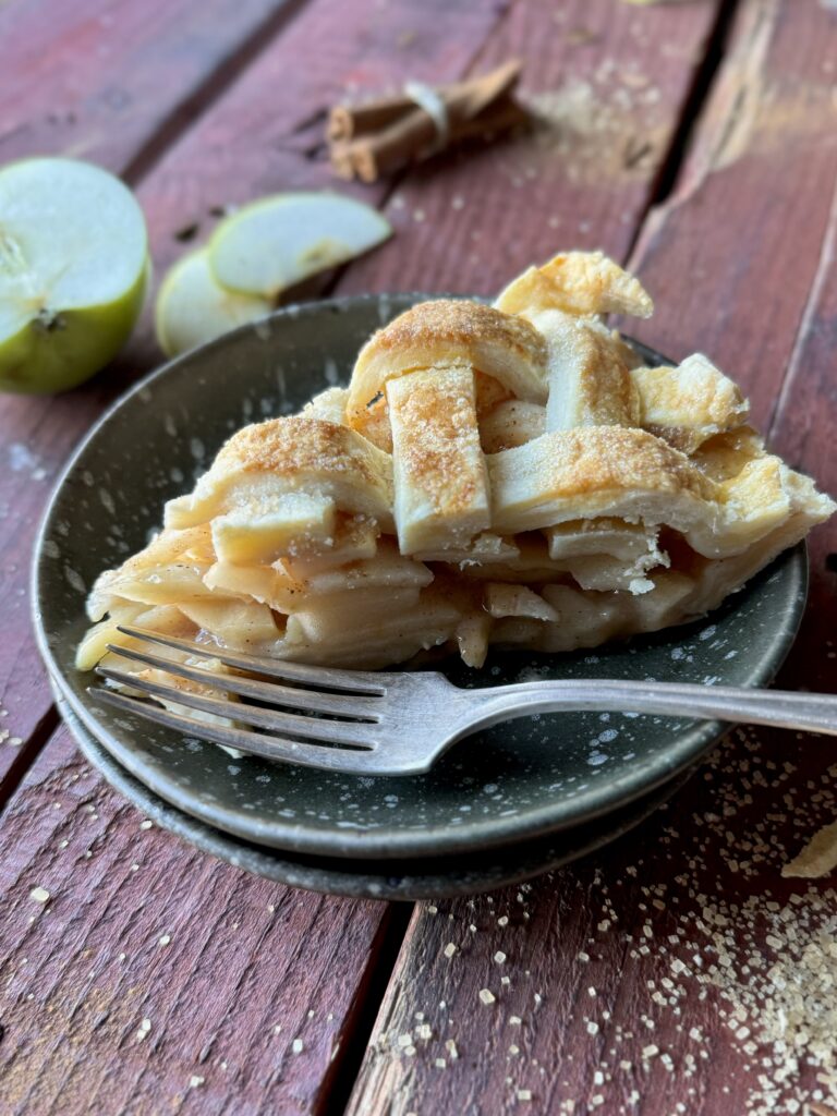 A slice of traditional apple pie with a lattice top crust on a plate with a fork.