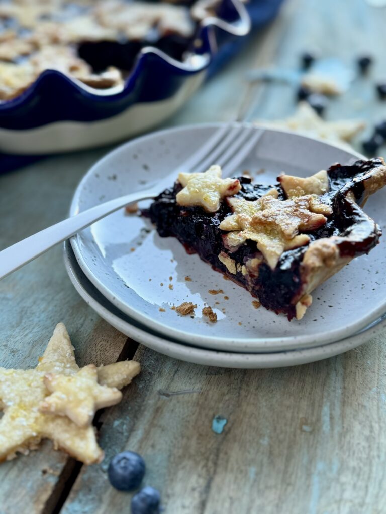 A slice of cherry blueberry pie with star crust on a white plate with a for,