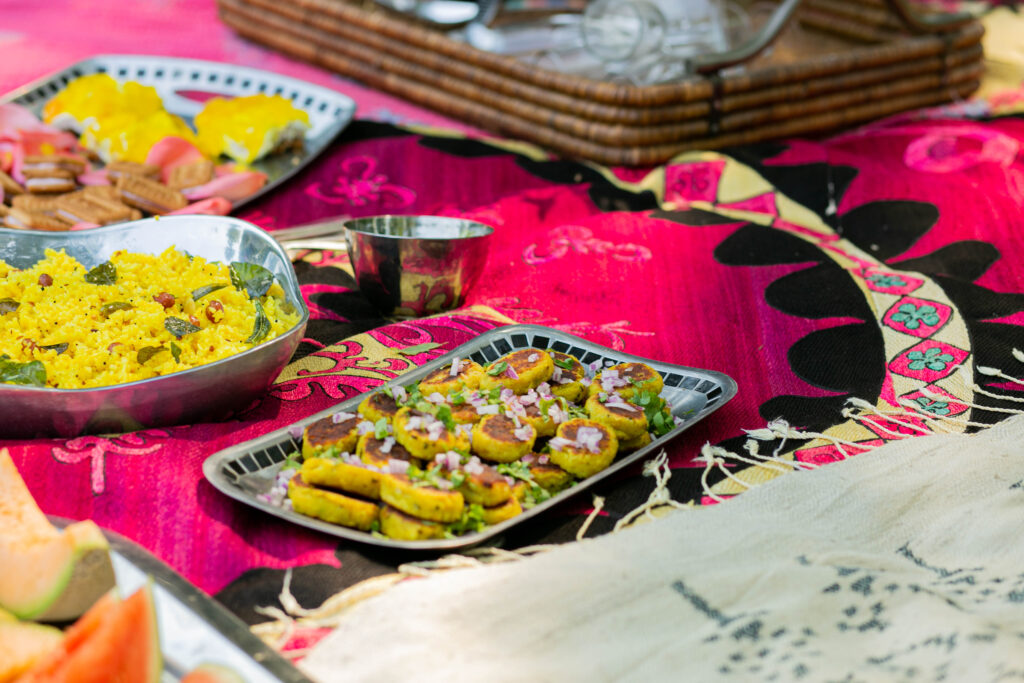A rectangular blue plate of Aloo Tikki sits on a pink pattern picnic cloth with other plates of food nearby.
