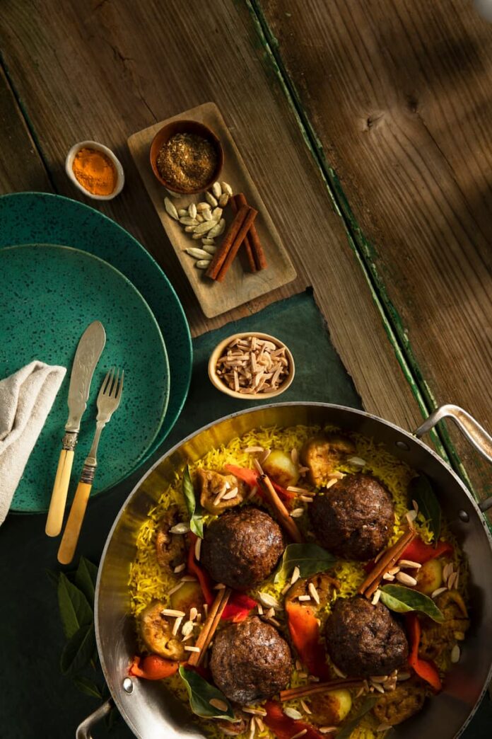 Maqluba (Makloubeh) with Lamb Meatballs served in a skillet, two plates, a fork & a spoon, and some herbs