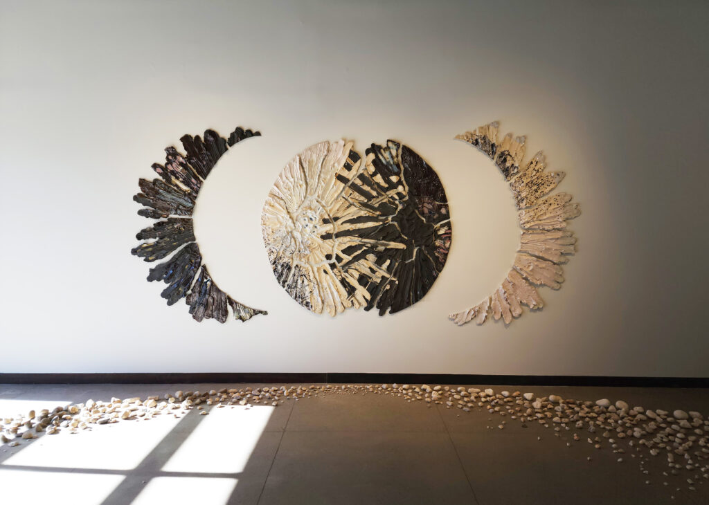 A piece from oneness by Brie Ruais is pictured, two heaps of white and black clay make two crescent moons before combining into one bigger moon with rocks littered beneath it.