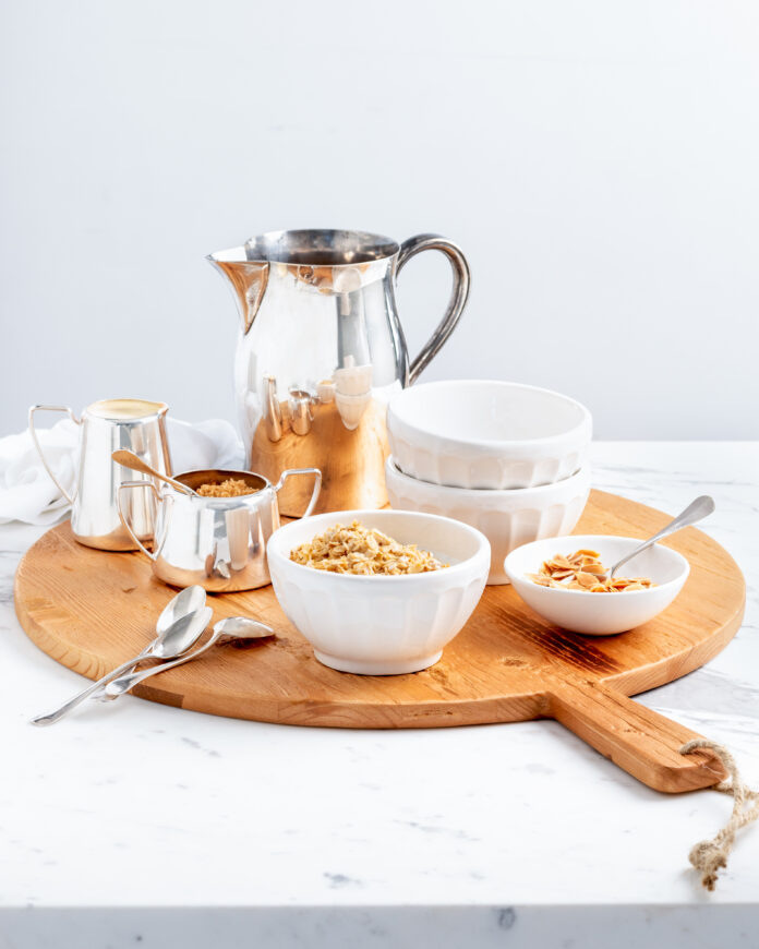 A wood servings tray platter holds a pitcher with various white bowls and silver spoons by Hudson Grace.