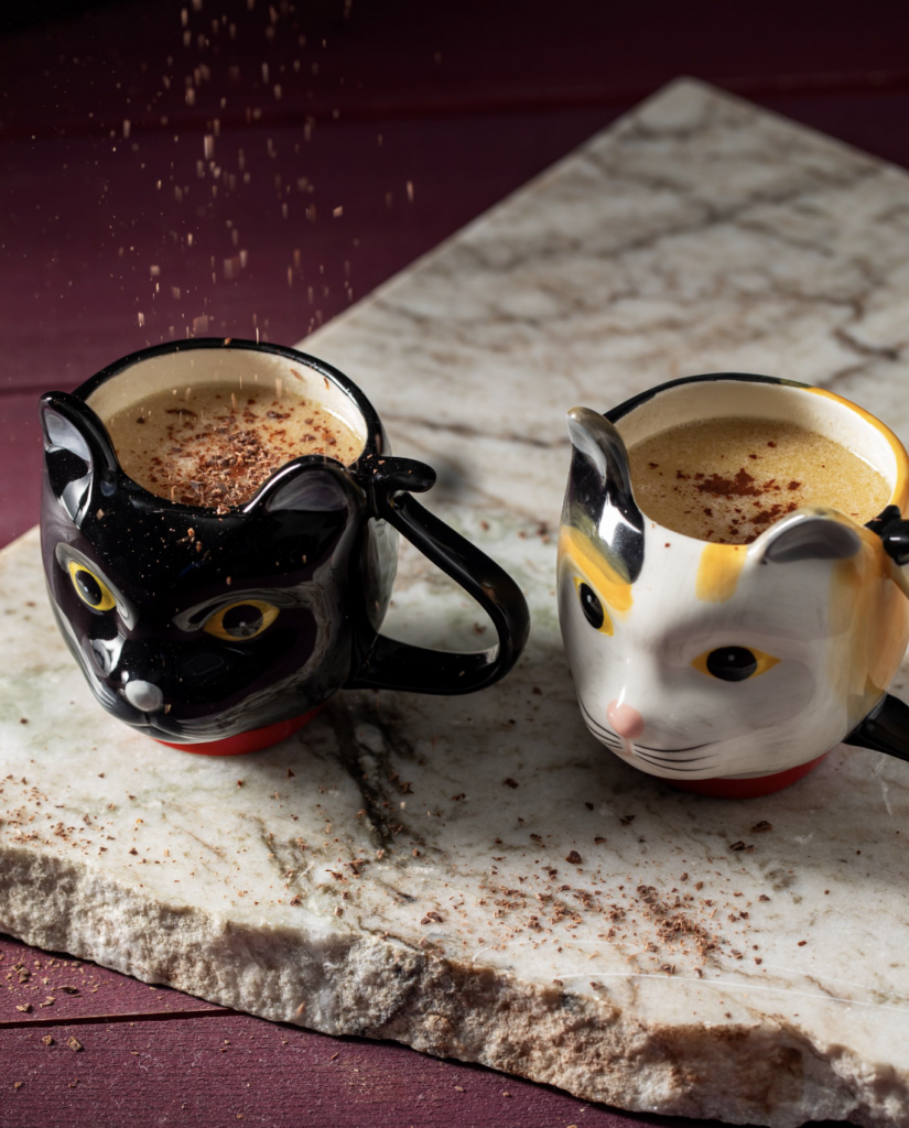 Two cat shaped mugs sit with a Melt Your Heart Valentine's Day cocktail in each and topped with ginger.