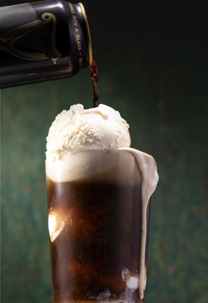 A closeup look in photo of a Guinness Beer Float with vanilla ice cream and a can of beer being poured over the top of a ball of creamy white ice cream.