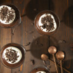 Chocolate Cremeux - pudding served in four glasses with chocolate chunks spread across the wooden table alongside three spoons