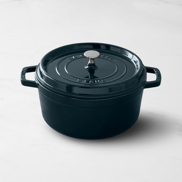 A deep black colored pot sits on a white table showing cookware from the Staub collection.