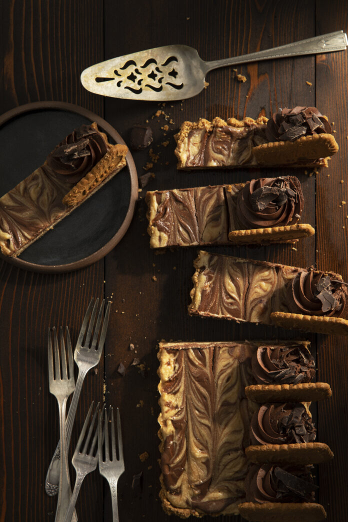 Peanut butter chocolate cheesecake sliced and served on a wooden surface with forks on the side