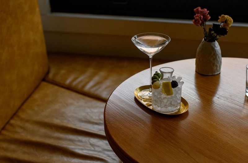 A cocktail martini glass sits on a wooden table with a shorter cocktail glass beside it. 