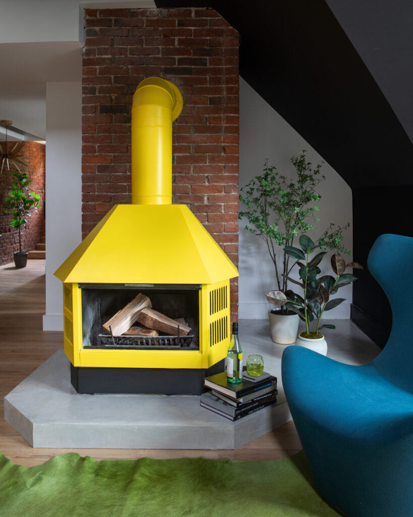 A yellow fireplace sits in a living room with a bright teal chair in the corner and decorations all around.