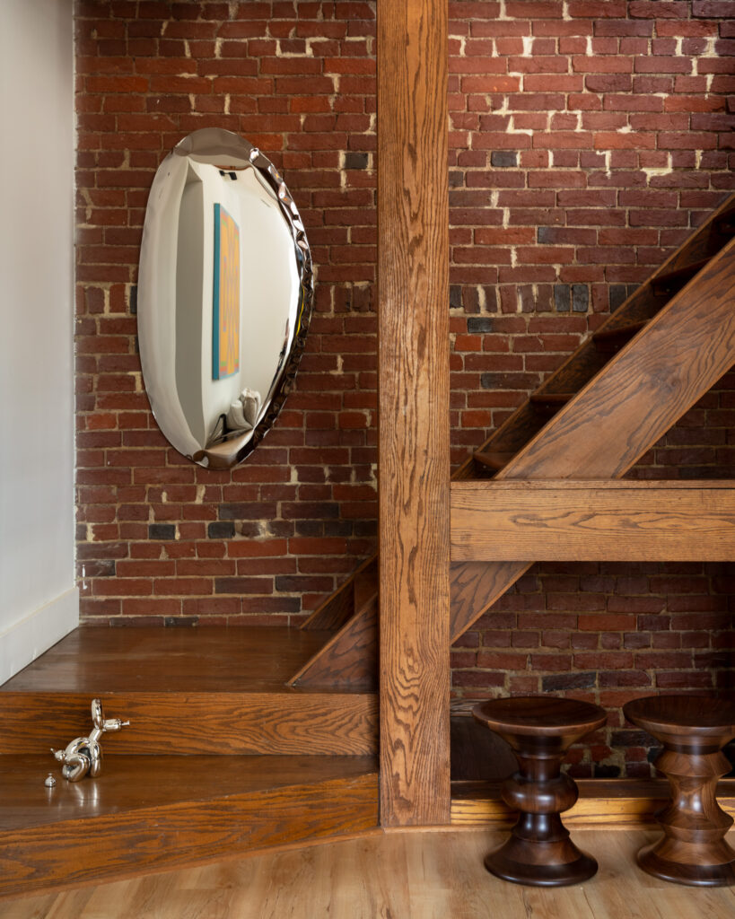 A brick wall sits behind a wooden staircase with a metallic silver sculpture on the wall and on the stair.