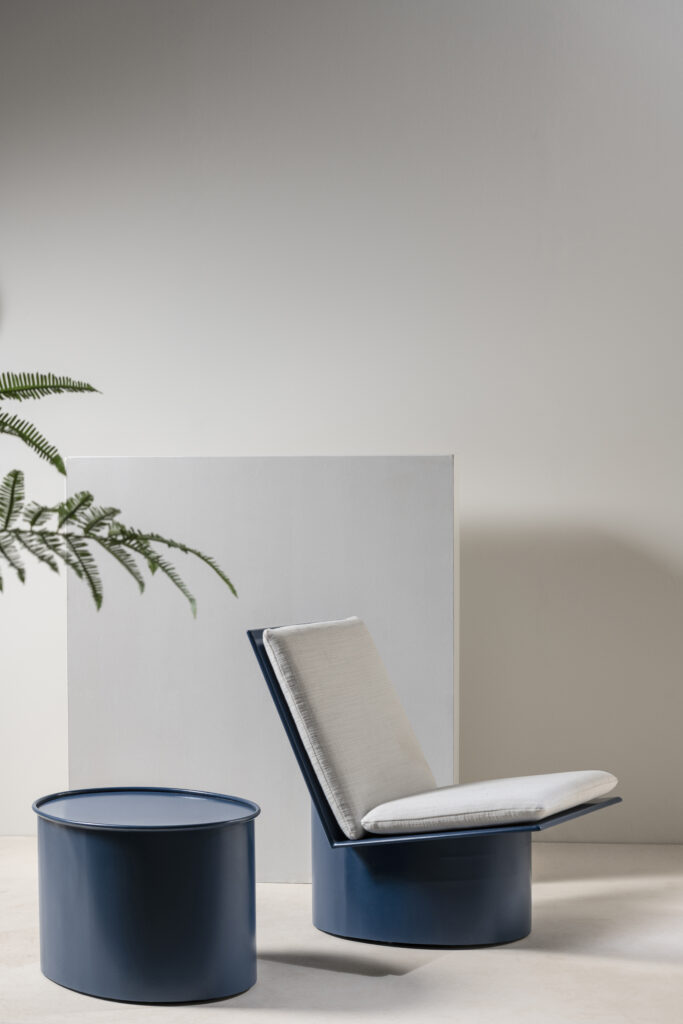 A blue lounge chair sits beside a blue side table in a minimalist white room.