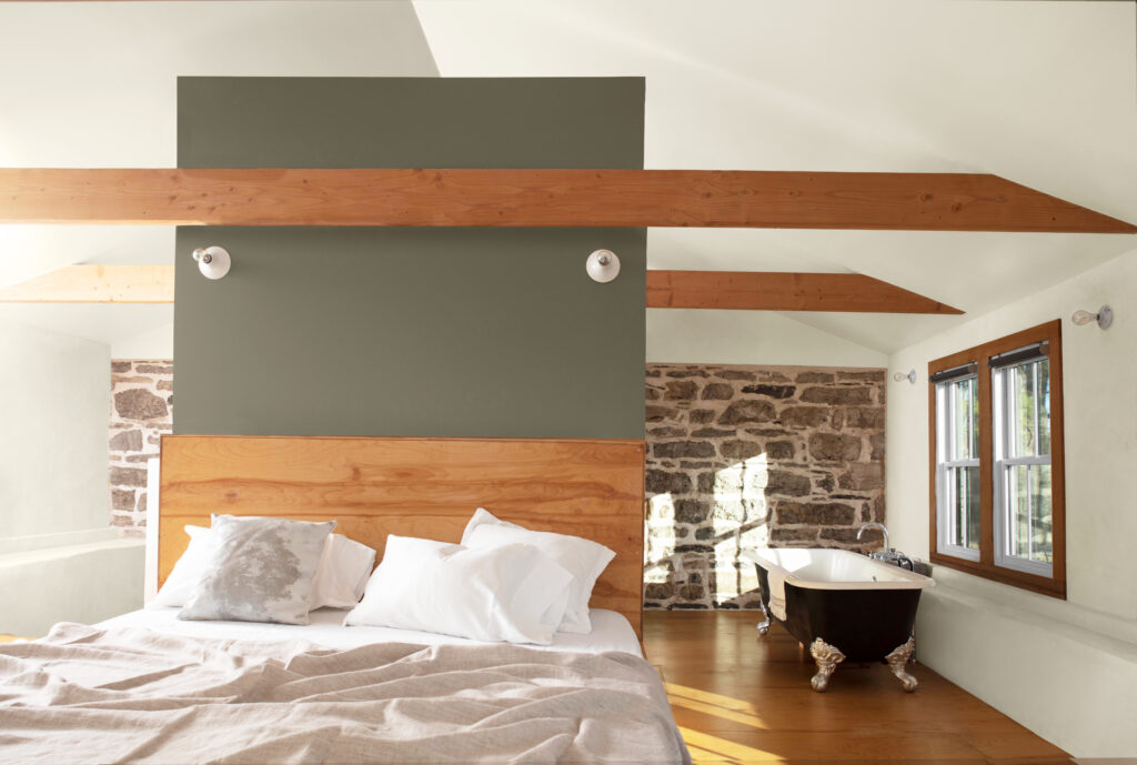 A bed room with wooden boards behind the bed and a dark pale green paint behind it as well.