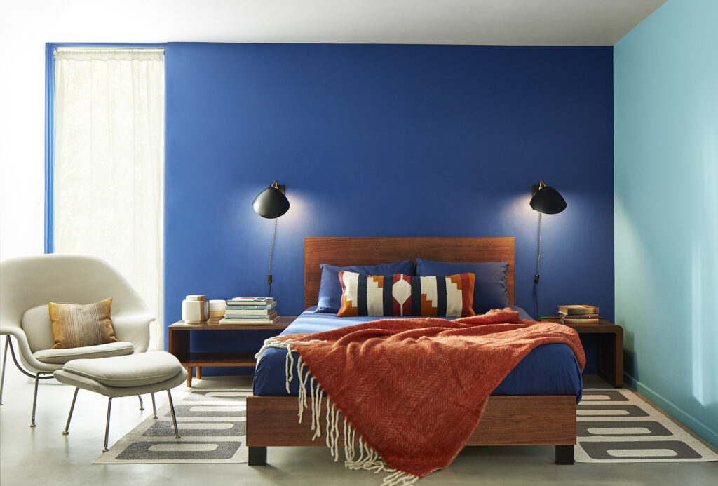 A bedroom with a dark blue wall behind a bed that has dark blue sheets to match.