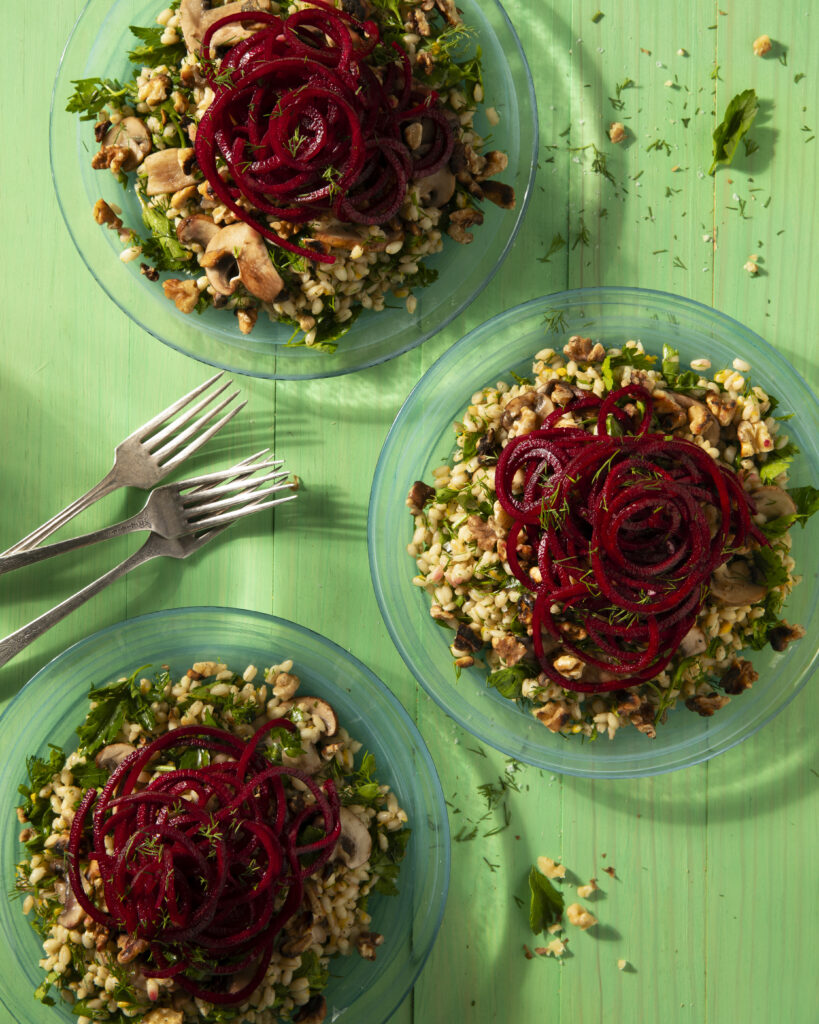 Three clear plates hold Barley Salad with Walnuts and Beets on a green background
