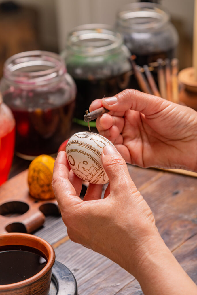 A person paints wax onto an egg to make Pysanky designs before dyeing.