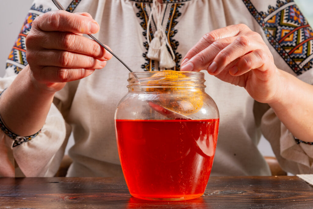 A woman uses a spoon to dip an egg into natural red dye in a jar.