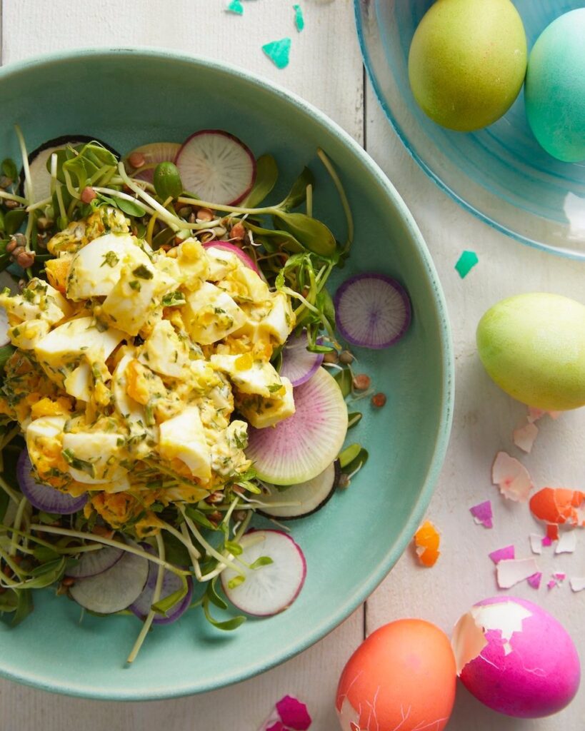 A green bowl holds a Green Goddess Egg Salad with dyed eggs to the right of the bowl.