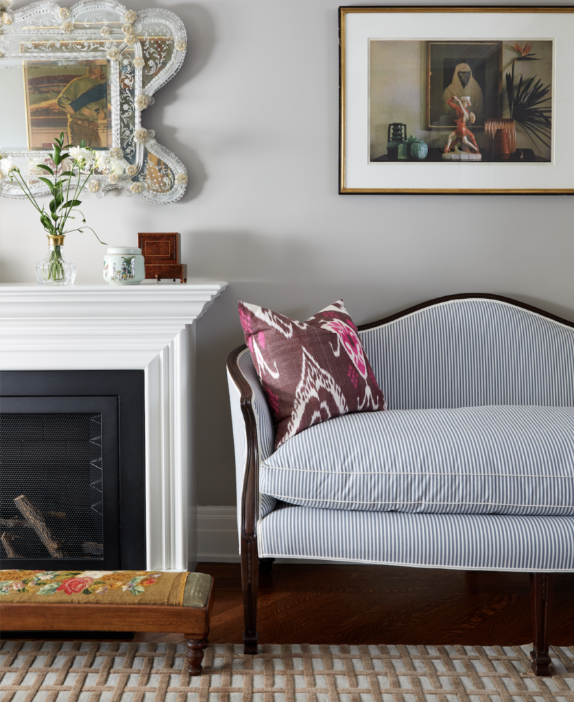 A pale blue couch sits next to a fireplace. Artwork hangs on the above wall.
