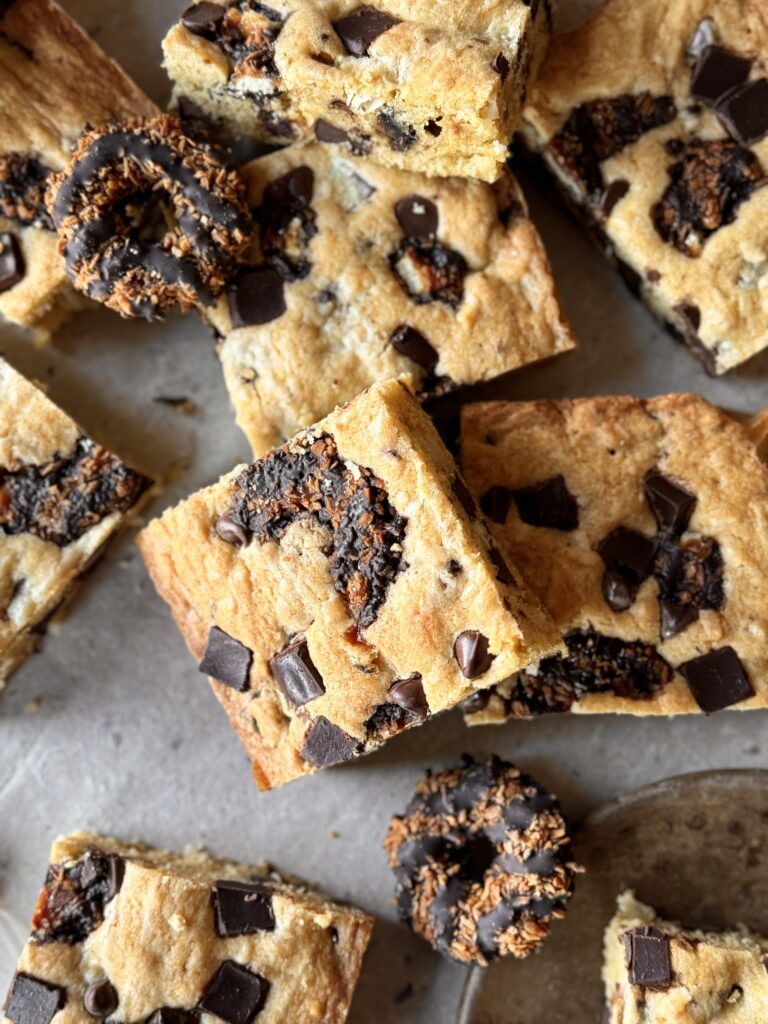 A pile of Samoas Blondies lay on a marble table top with lightly toasted tops.