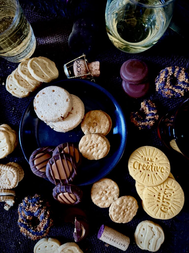 A variety of Girl Scout Cookies sit around different glasses of wine and wine corks.