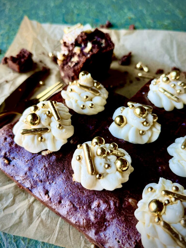 A 3/4 look in photo of Guinness brownies with white buttercream icing and gold sprinkles on a piece of parchment paper and a green surface.
