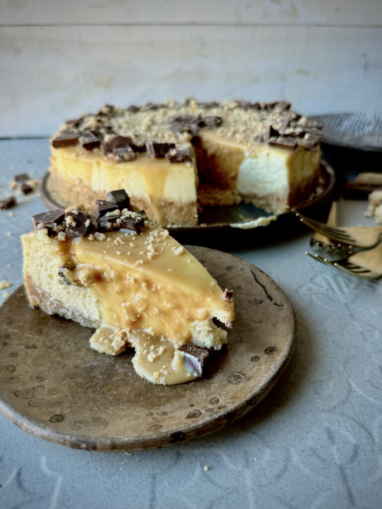 A look-in slice of cheesecake with caramel sauce and chocolate pieces.