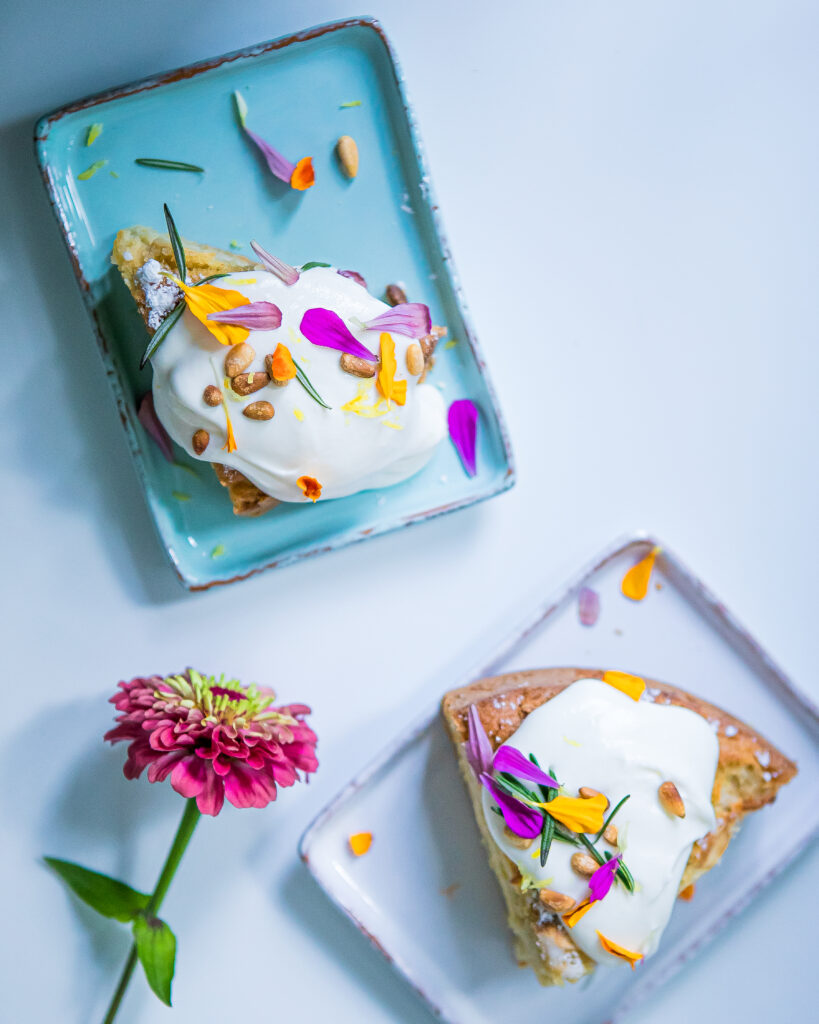 Two rectangular plates in blue and light purple hold a scoop of white cream with flower leaves scattered on top.