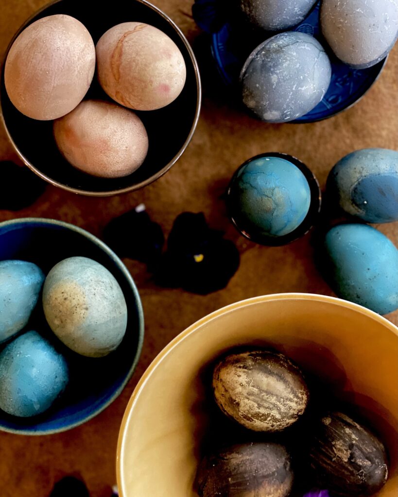 Different naturally dyed Easter Eggs sit in the bowls in the colors pink, purple, blue, and brown.