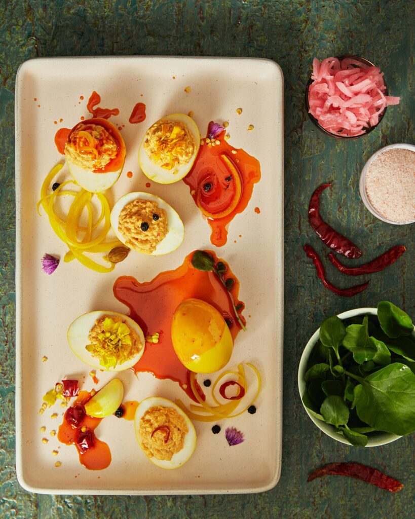 A white plate holds an array of chicken tikka deviled eggs covered in an orange chili oil.