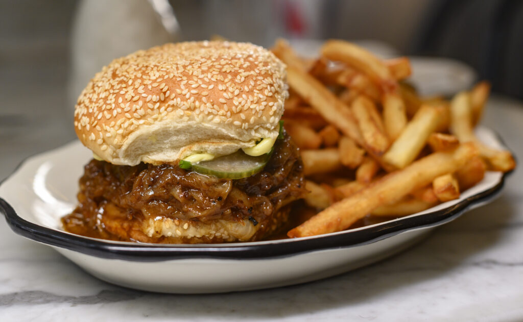 A sandwich with pickles and a seeded bun sits on a plate next to a side of french fries.