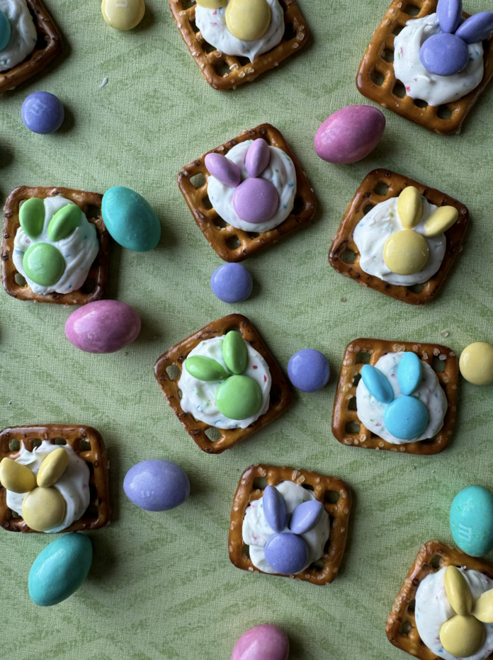 Chocolate Pretzel Easter Bunny Treats Chocolate Pretzel Easter Bunny Treats sit on a green striped background made out of pretzels, chocolate, and M&Ms with M&Ms tossed between the treats.