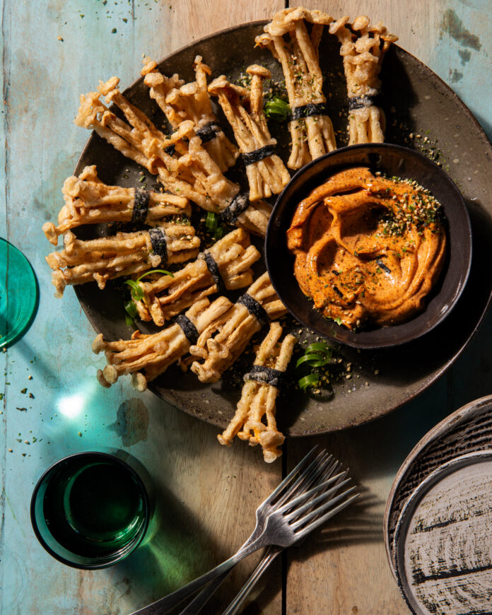 Crispy Mushroom Bundles Various crispy mushroom bundles sit on a brown plate beside a small bowl of spicy mayo beside two green cups and two forks.