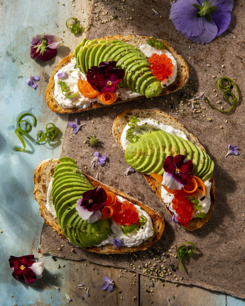 three slices of toast sit with perfectly slices pieces of avocado, cheese, and carrots.