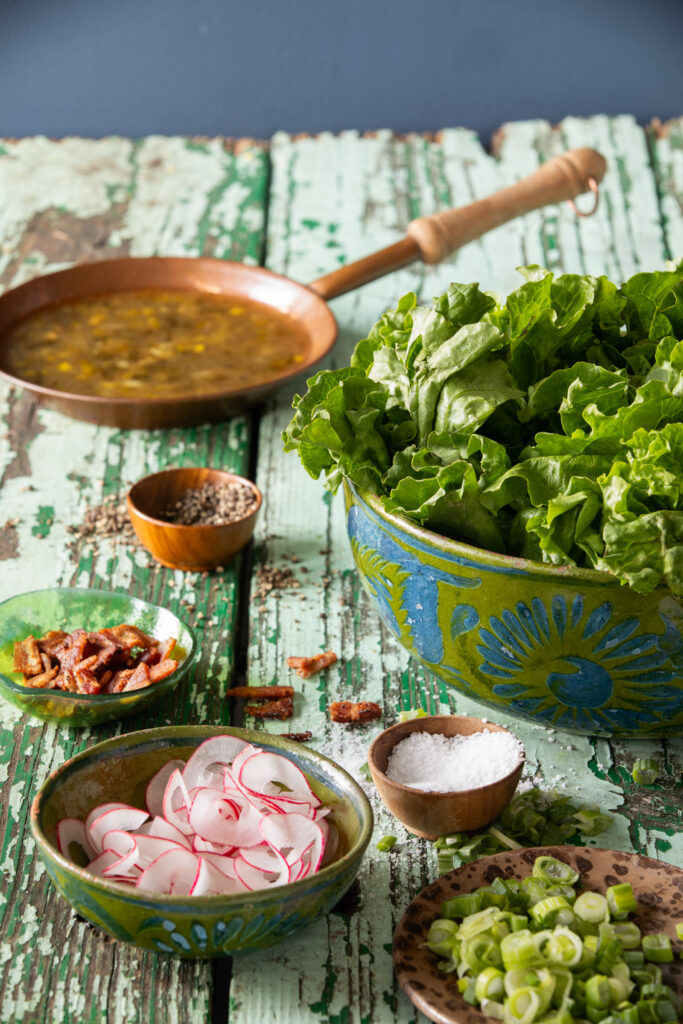 Wilted Lettuce Salad - A bowl of fresh leaf lettuce topped with crispy bacon, radishes, and scallions