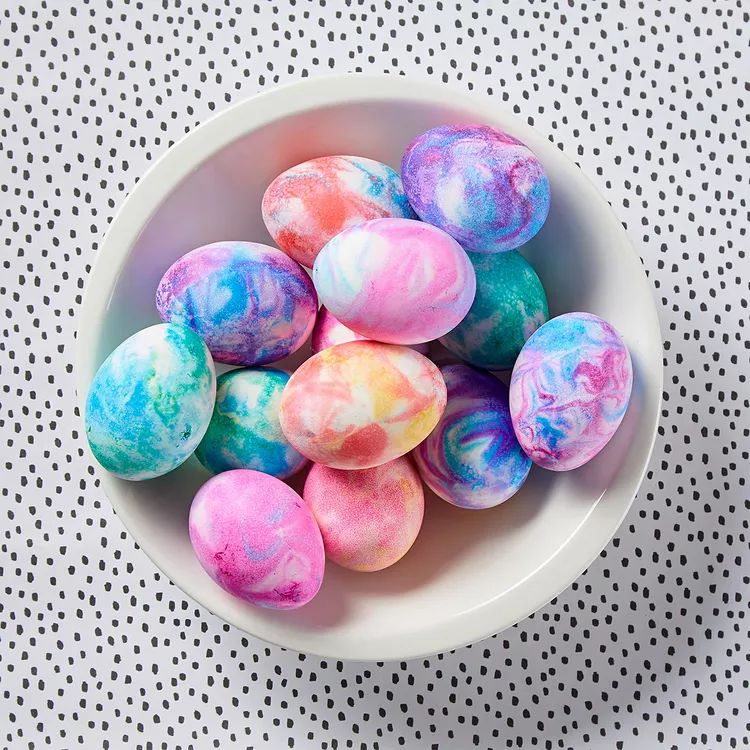 A white bowls holds various colorful marbled dyed Easter eggs.