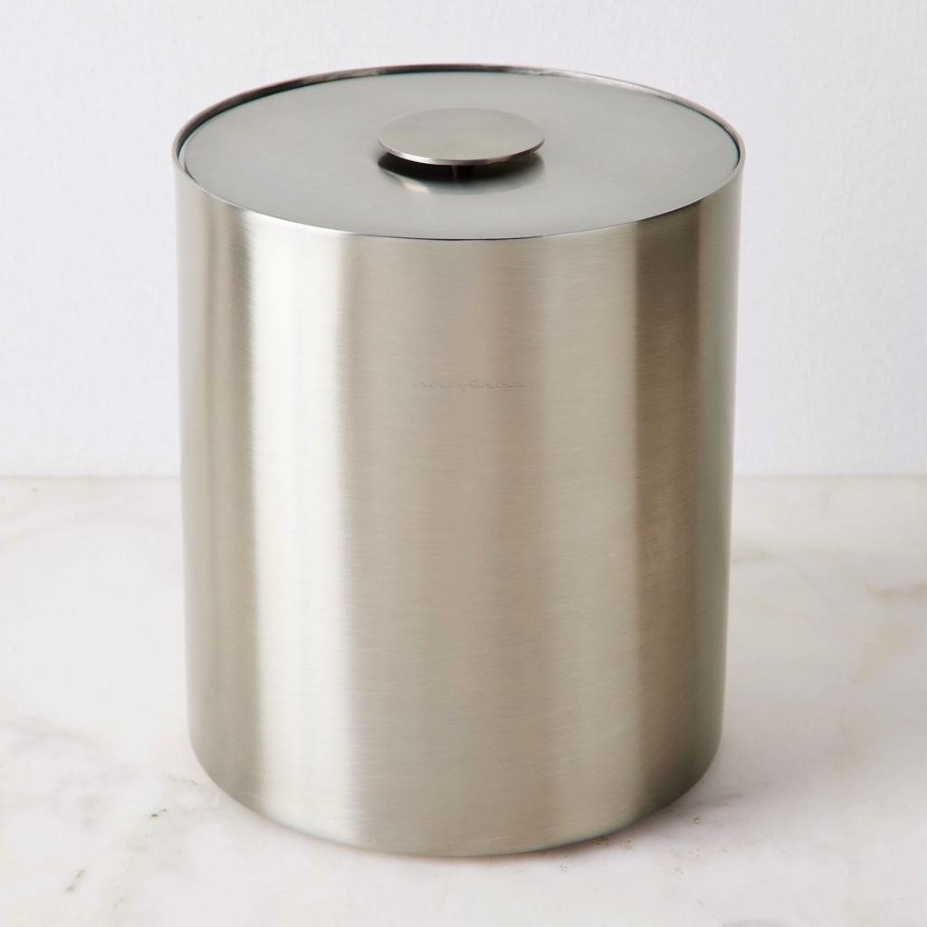 A stainless-steel ice bucket with a smooth top sits on a beige backdrop.