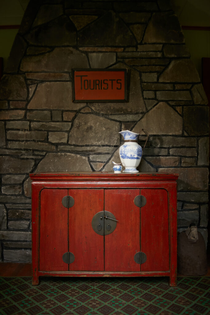 A red cabinet with a white and blue vase on top and a red sign above it all on a stone wall.