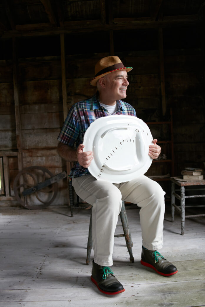 Andrew Baseman sits in a chair holding one of his repaired platters in his lap.
