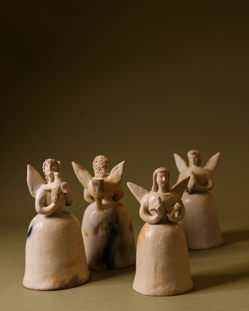 A group of four ceramic beige angels sit on a greenish brown background.