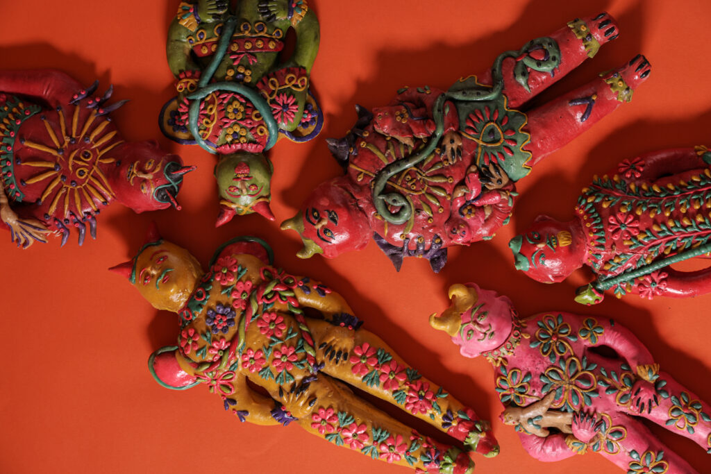 Six devils created in what looks like a bread dough material sit against a bright orange background at the Museum of International Folk Art.