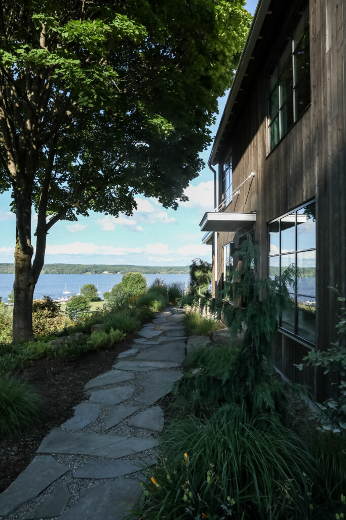 The side of a Chautauqua Lake House with a stone path under a tree leading down to the lake.