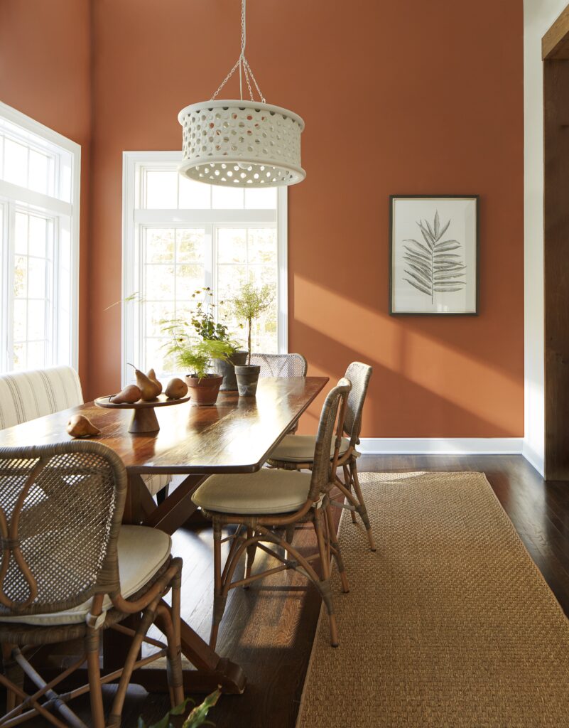 A dining room with burnt orange walls and white windows plus a brown table and chairs.